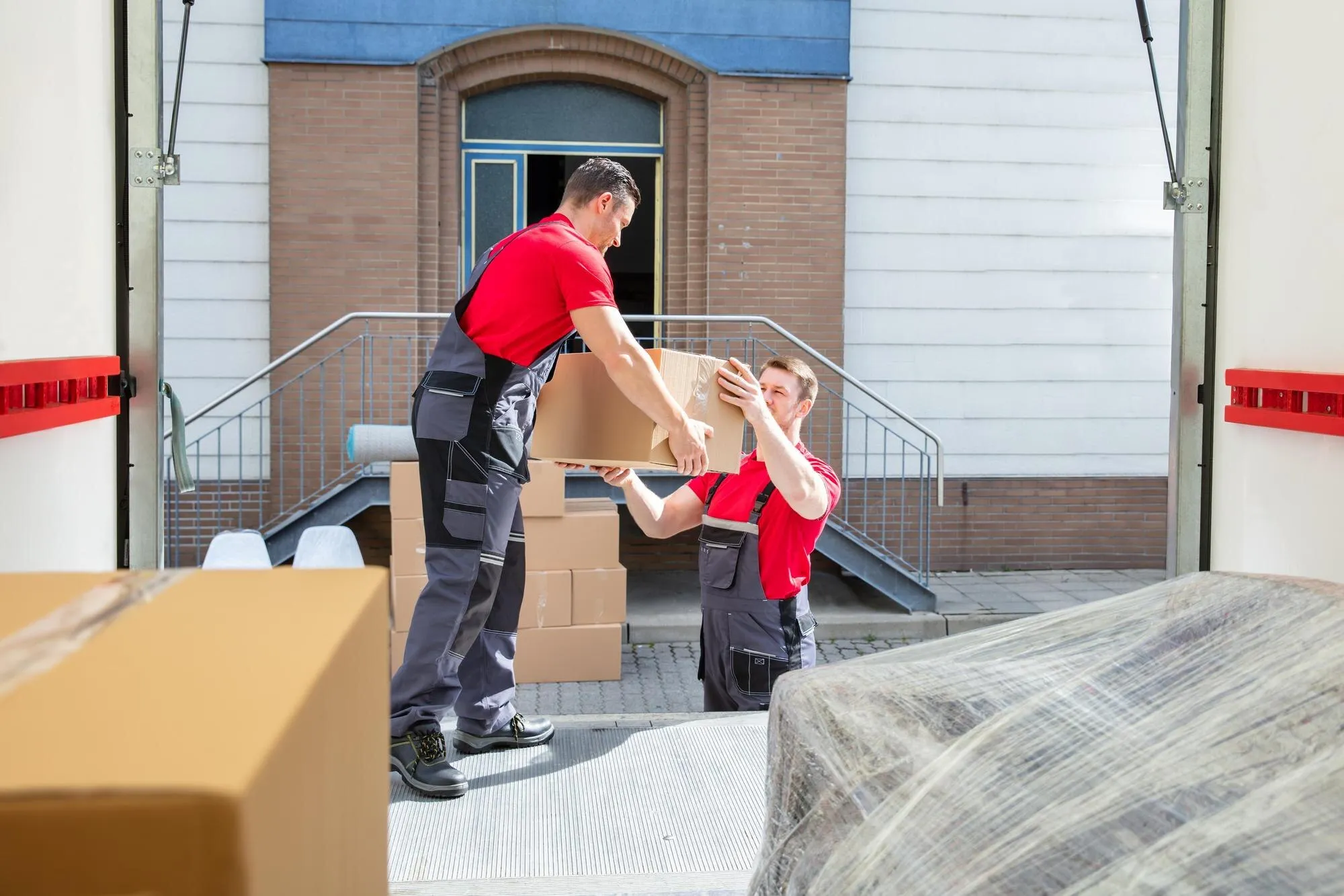 Zwei Umzugshelfer beladen einen Umzugswagen vor einem Haus