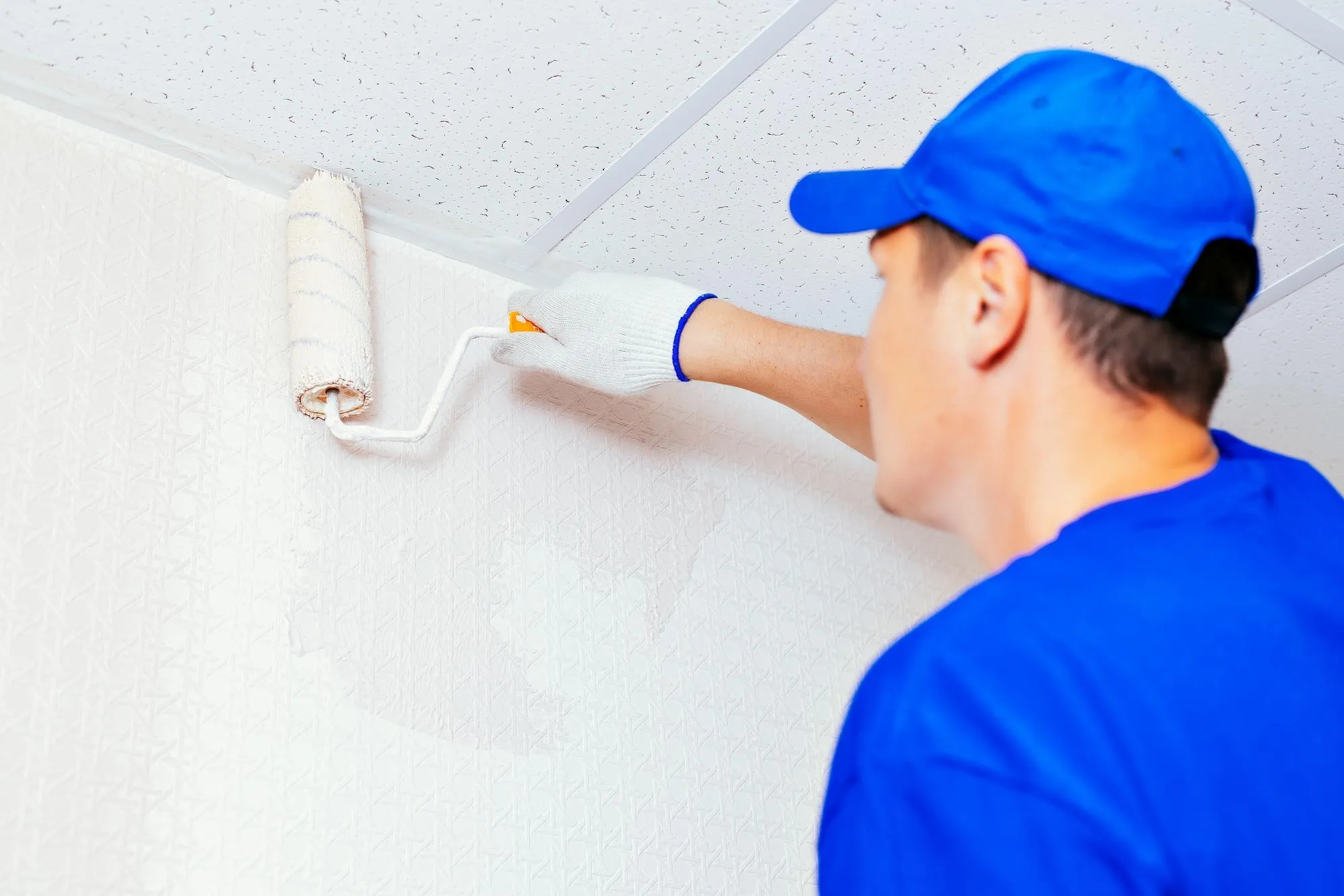 Ein Maler streicht eine Wand mit der Farbrolle weiß
