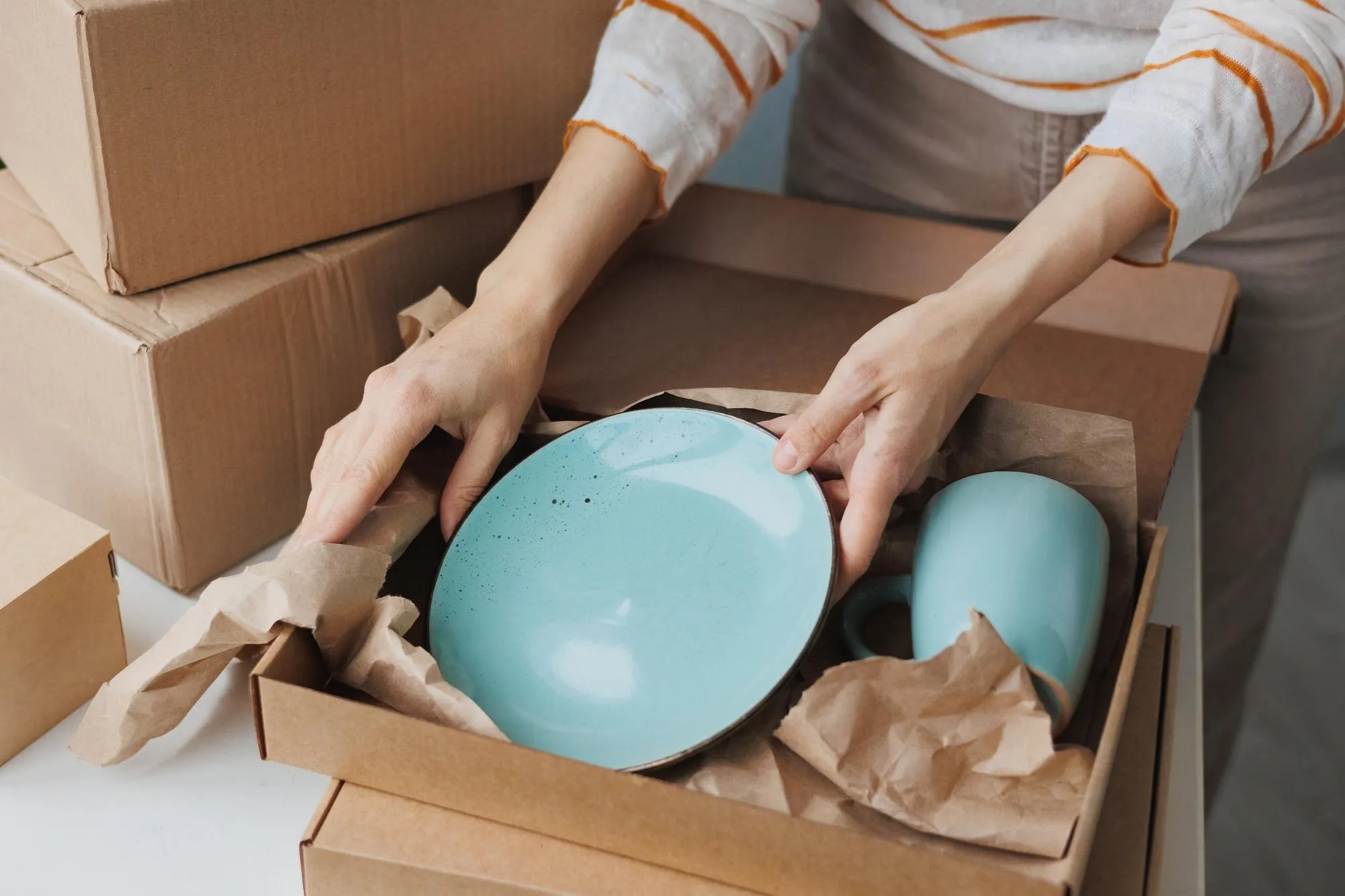 Geschirr wird sorgfältig in Papier eingeschlagen und in einen Karton gepackt